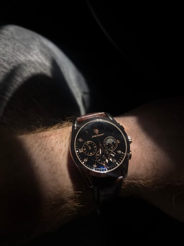 Close-up of a customer wearing the Lucky Fours® Voyager watch, showing its dark face and silver case in shadow.