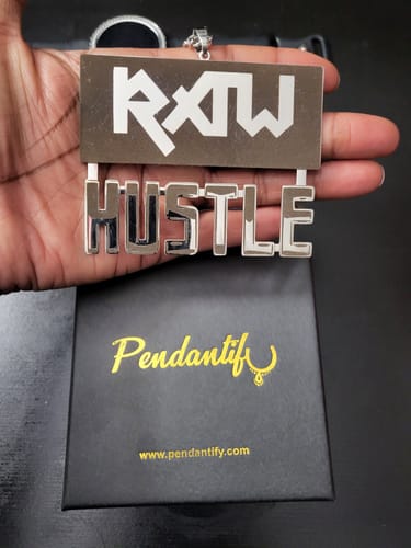 Customer holding a large silver-colored custom pendant that reads 'RXTW HUSTLE' over its black 'Pendantif' gift box.