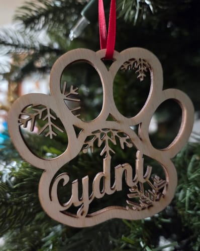 Customer's personalized wooden pet ornament in a paw print shape, customized with the name 'Cydni' and hanging on a tree.