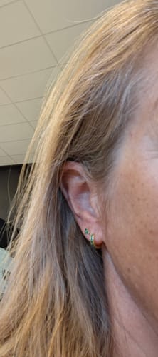 Close-up of a reviewer's ear showing two gold earrings, one a small hoop and the other a stud with green stones.