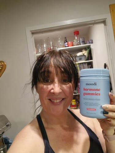 Customer smiling while holding a light blue jar of Strawberry Hormone Gummies.