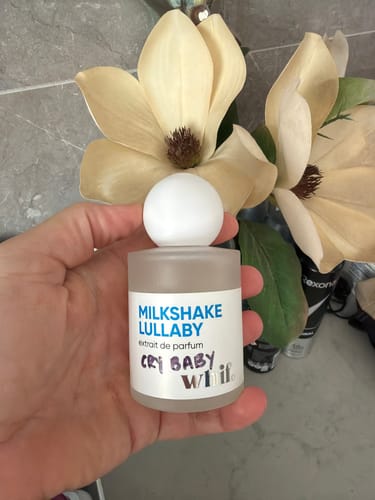 Customer's hand holding the small, frosted bottle of Milkshake Lullaby perfume in a bathroom setting.