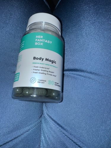 Customer's bottle of Body Magic dietary supplement capsules resting on a blue fabric surface.