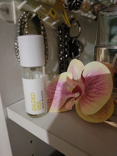 Customer's mini Gilded Veil perfume bottle on a vanity shelf next to a flower.