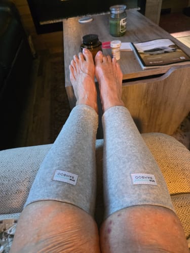 Reviewer relaxing with their feet up, wearing the light grey Premium Bamboo Anti-Fatigue Calf Sleeves on both legs.