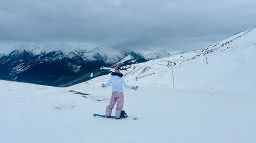 Reviewer from behind wearing the glossy snow pants while on a snowboard on a snowy mountain.