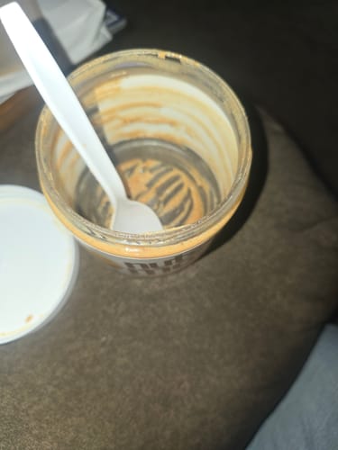 A reviewer's empty jar of Salted Caramel High Protein Peanut Butter Spread, completely scraped clean with a spoon inside.