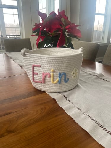 Customer's personalized Baby Knits basket with the name 'Erin' in multicolor yarn and a flower icon on a table.