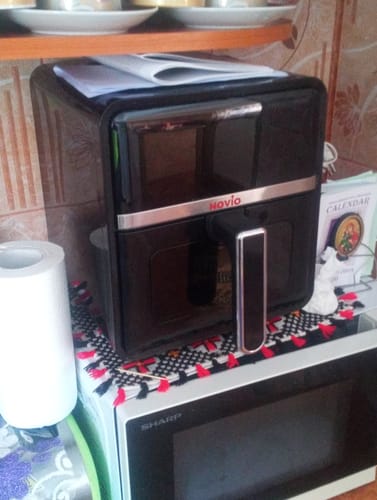 Imagine de la client cu air fryer-ul negru Novio StonePro, așezat pe un cuptor cu microunde în bucătărie.