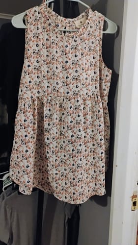 Customer's Mini Blooms Peplum Tank with a floral print and ruffled neckline hanging in a closet.