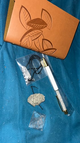 Customer's AuraBloom Subscription Box items, featuring a tan journal, a pen, and spiritual crystals.