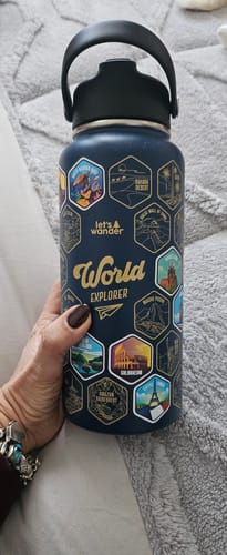 A reviewer's hand holding the dark blue World Explorer Bottle, showing several colorful stickers placed on it.