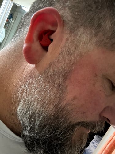 Close-up of a reviewer's ear with a red X20 Earplug inserted, showing the product's fit.