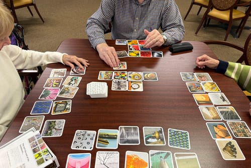 Customers playing the OuiSi Getty card game at a wooden table, with many art cards laid out.