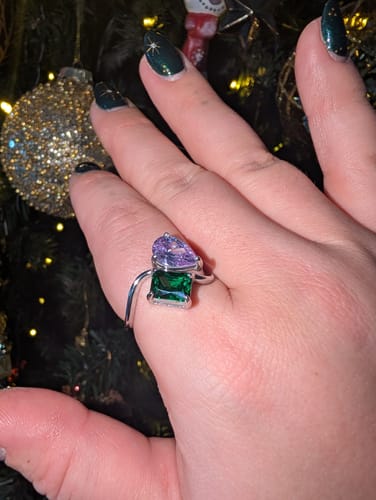 A customer's hand wearing the Navae Birthstone Ring with a purple pear-cut and a green radiant-cut stone.