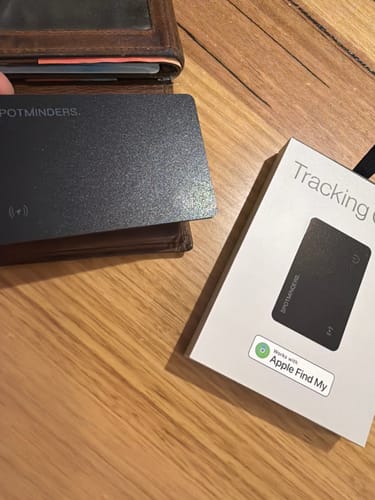 Customer holds the SPOTMINDERS Tracking Card by a wallet, with its white packaging shown on a wooden table.