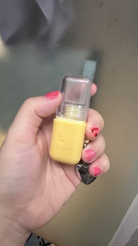 Customer's hand holding the Deep Hydration Lip Oil in its compact, yellow container with a clear cap.