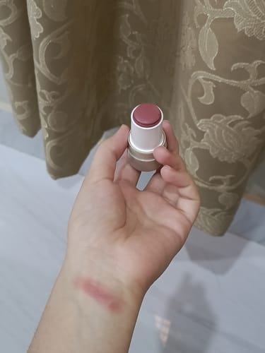 Reviewer holding the open VELVET FLUSH blush stick with a swatch of the rosy color on their wrist.