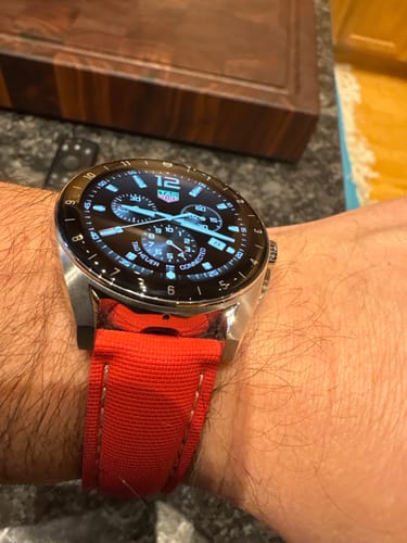 A customer's wrist wearing the red Sailcloth Rubber Deploy strap on a silver chronograph watch.