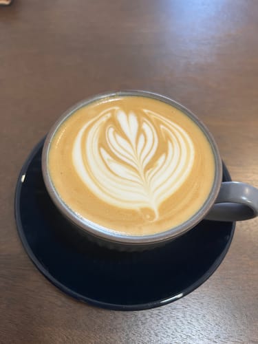 Customer's cup of Bali Kintamani coffee prepared as a latte with detailed foam art in a grey mug on a black saucer.