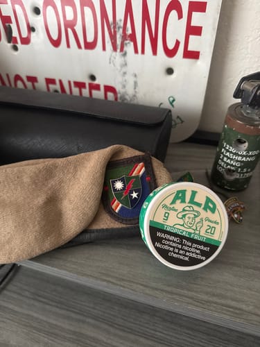 A customer's can of ALP Tropical Fruit pouches on a wooden surface with military memorabilia in the background.