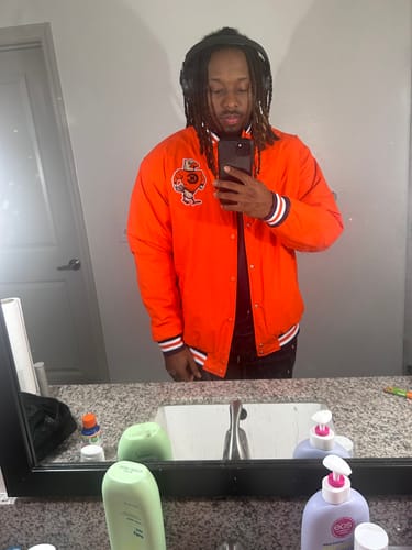 Customer taking a mirror selfie while wearing the bright orange Custom Letterman Varsity Jacket.