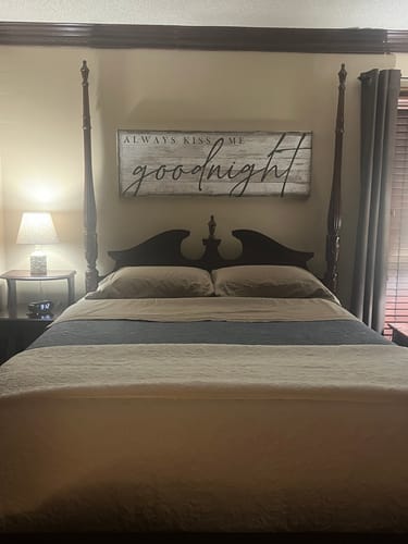 Customer's 'Always Kiss Me Goodnight Bedroom Sign II' mounted on the wall above their four-poster bed.