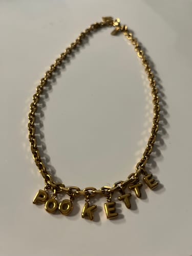 Customer's gold-colored Bubble Letter Name Necklace with the name 'POOKETTE' laid out on a white surface.