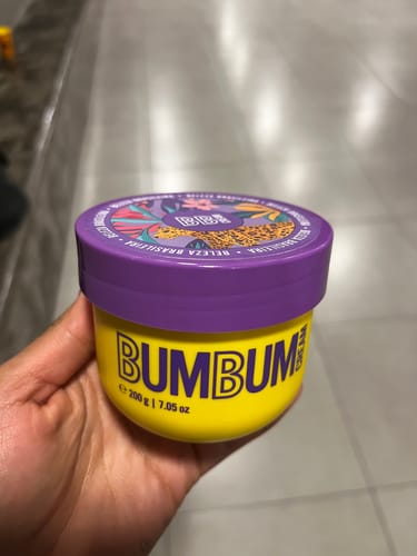 Cliente segurando o pote amarelo do produto Bumbum Cream com tampa roxa.