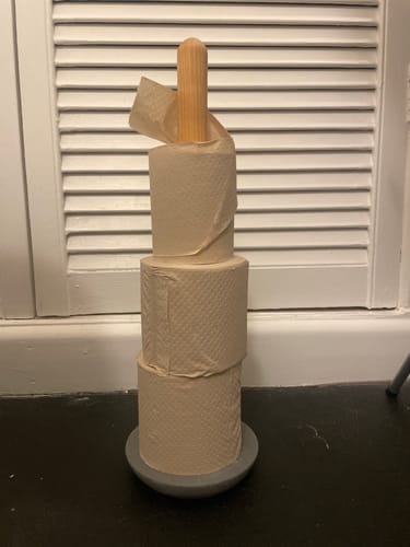 Customer's three stacked rolls of Unbleached Bamboo Toilet Paper on a wooden and grey floor stand.