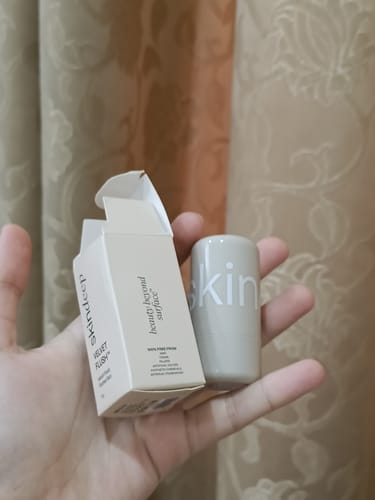 Customer holding the VELVET FLUSH blush stick and its small box in their hand against a curtain.