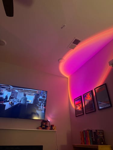 Reviewer's living room showing the Golden Hour Sunset Lamp projecting a vibrant pink and yellow light on the wall and ceiling.