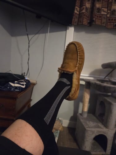 Customer's leg with a black Men's Alpaca Sock pulled up to the knee while wearing a slipper.