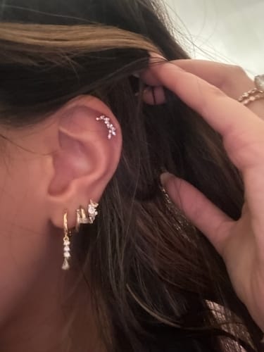 Close-up of a customer wearing the gold Cluster huggies with clear stones as part of an ear stack.