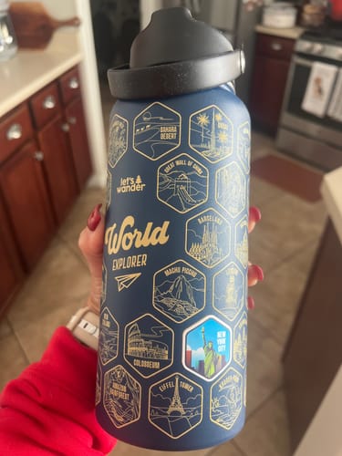 Customer holds the blue World Explorer Water Bottle, showing gold landmark outlines and one applied New York City sticker.