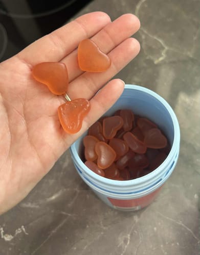 Customer holding three heart-shaped, orange Peach Hormone Gummies over the open product container.