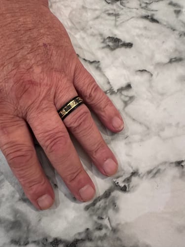 Customer's hand resting on a marbled surface, showing the black Titanfall ring with a gold flake and meteorite inlay.