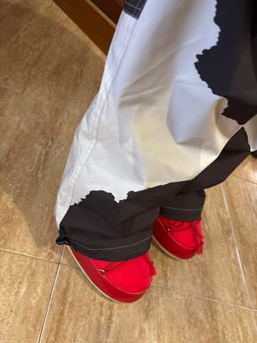 Close-up of the reviewer's Cow Print Snow Pants showing the uncinched, loose ankle cuff over red boots.