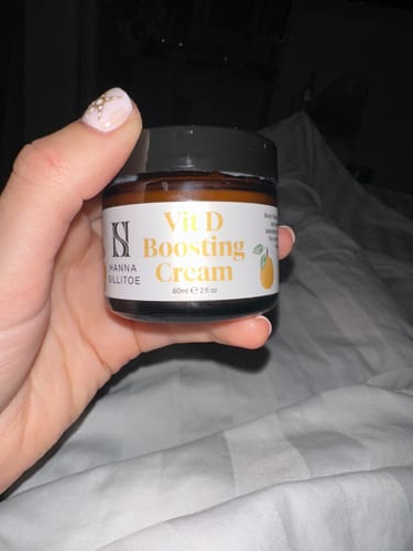 Customer holding the amber-colored jar of Vit D Boosting Cream against a white background.