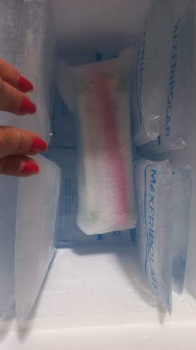 Cliente muestra su medicamento Prolia al recibirlo, en una hielera rodeado de bolsas de gel para mantenerlo frío.