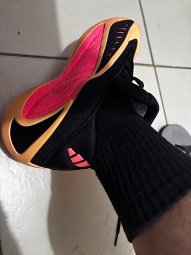 Customer wearing one adidas Anthony Edwards 2 basketball shoe, showing the bright pink and orange outsole.