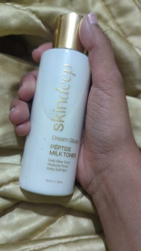 Reviewer's hand holding the white bottle of DREAM GLAZE Peptide Milk Toner with its gold cap.