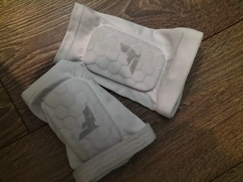 Reviewer's pair of white Built-In Shin Pads with hexagonal padding resting on a wooden surface.