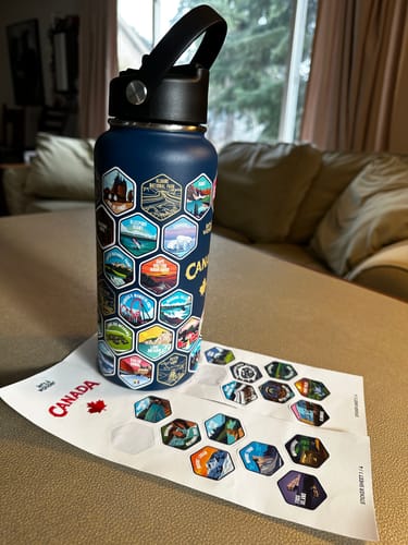 A customer's dark blue Canada Bottle on a table with many colorful stickers applied and sticker sheets nearby.