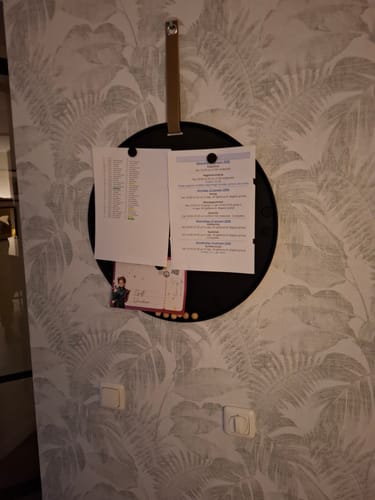 Recensent toont het zwarte, ronde Perky memobord dat aan de muur hangt met verschillende papieren erop.