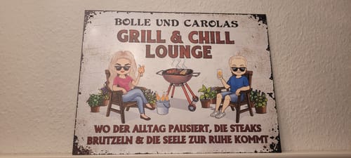 Kunde zeigt ein personalisiertes Gartenschild mit Avataren und dem Text „Bolle und Carolas Grill & Chill Lounge“.