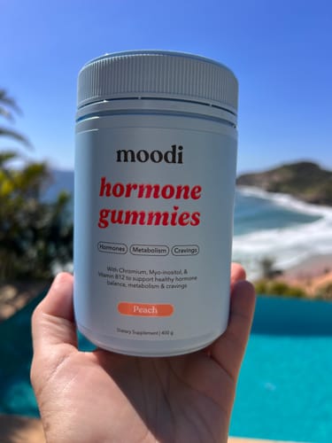 Customer holding a light blue jar of Peach Hormone Gummies in their hand by a sunny pool.