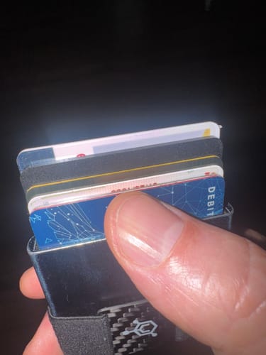 Close-up: Customer holding a dark aluminum wallet with the SPOTMINDERS Tracking Card placed among other cards.