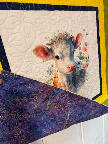 Close-up of a customer's quilt made with the Watercolor Cows fabric panel, lifting a corner to show the purple backing.