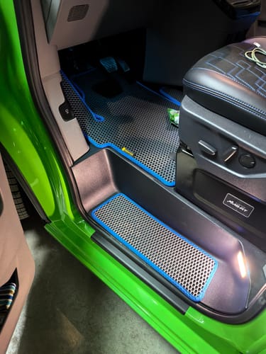 Recenzent pokazuje dopasowane dywaniki samochodowe, szare z niebieskim obszyciem, w swoim vanie.